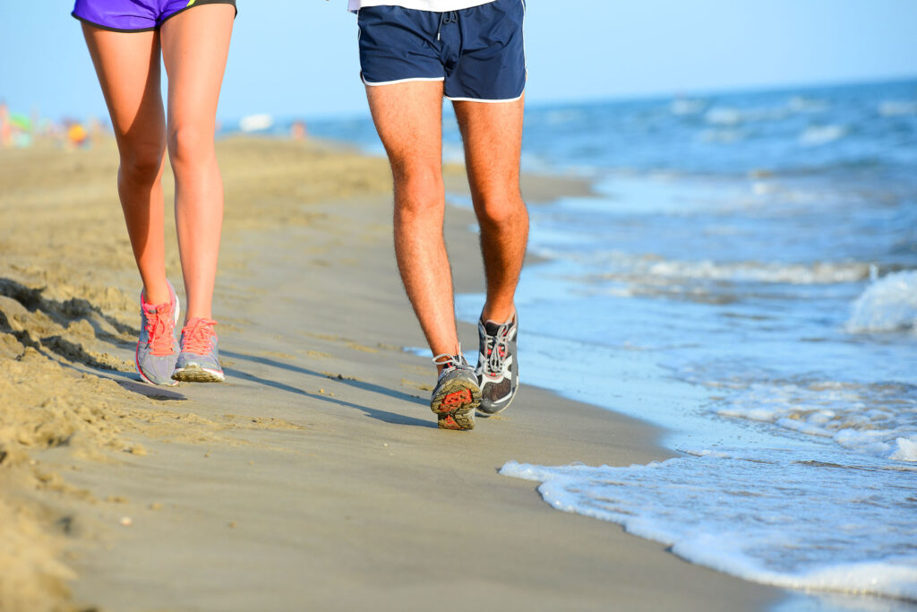 Couple jogging along beach shoreline to boost leg circulation and reduce varicose vein risk