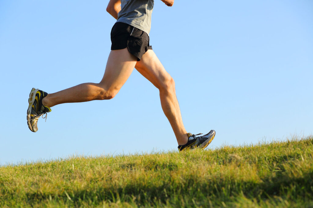 Side view of runner with muscular legs sprinting on grass