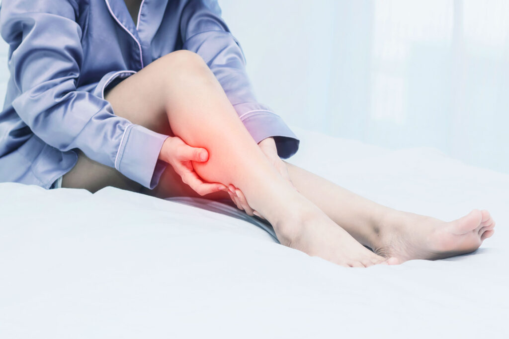 Woman sitting in bed grasping painful calf area