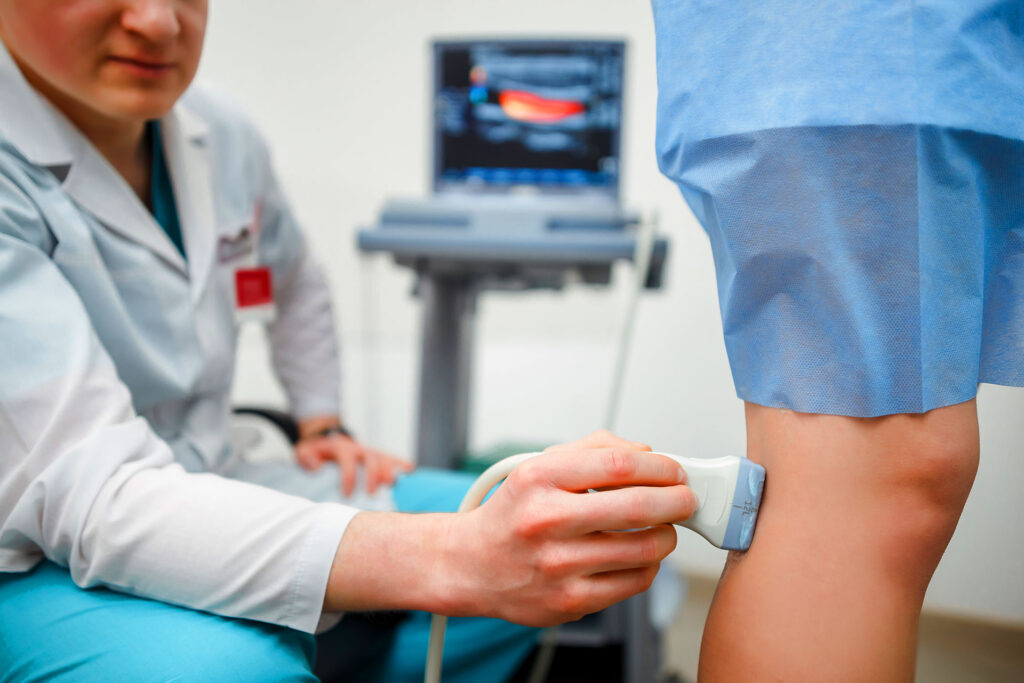 Doctor performing vein ultrasound scan on patient leg