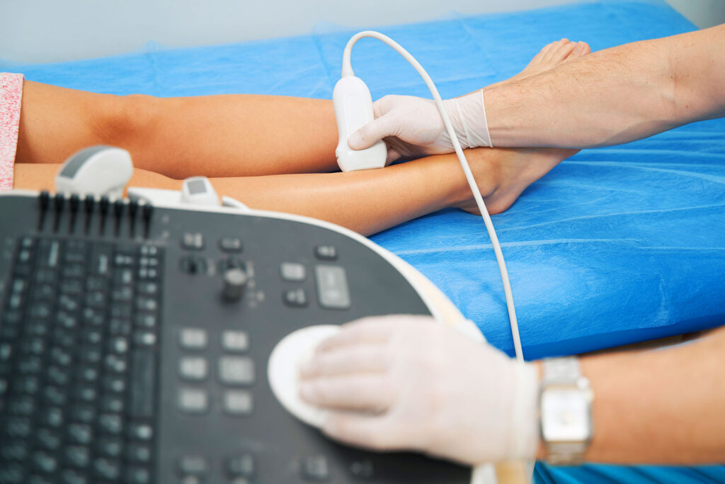 Medical professional examining a patient's lower leg using an ultrasound diagnostic machine.