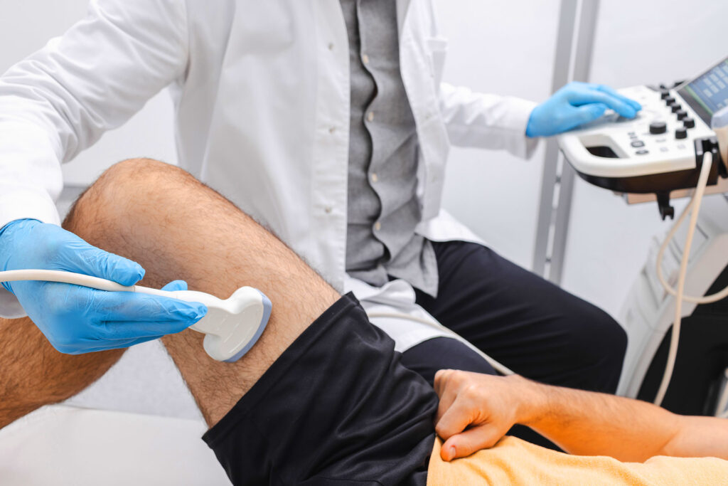 Doctor in blue gloves performing a leg ultrasound scan using a medical diagnostic machine.