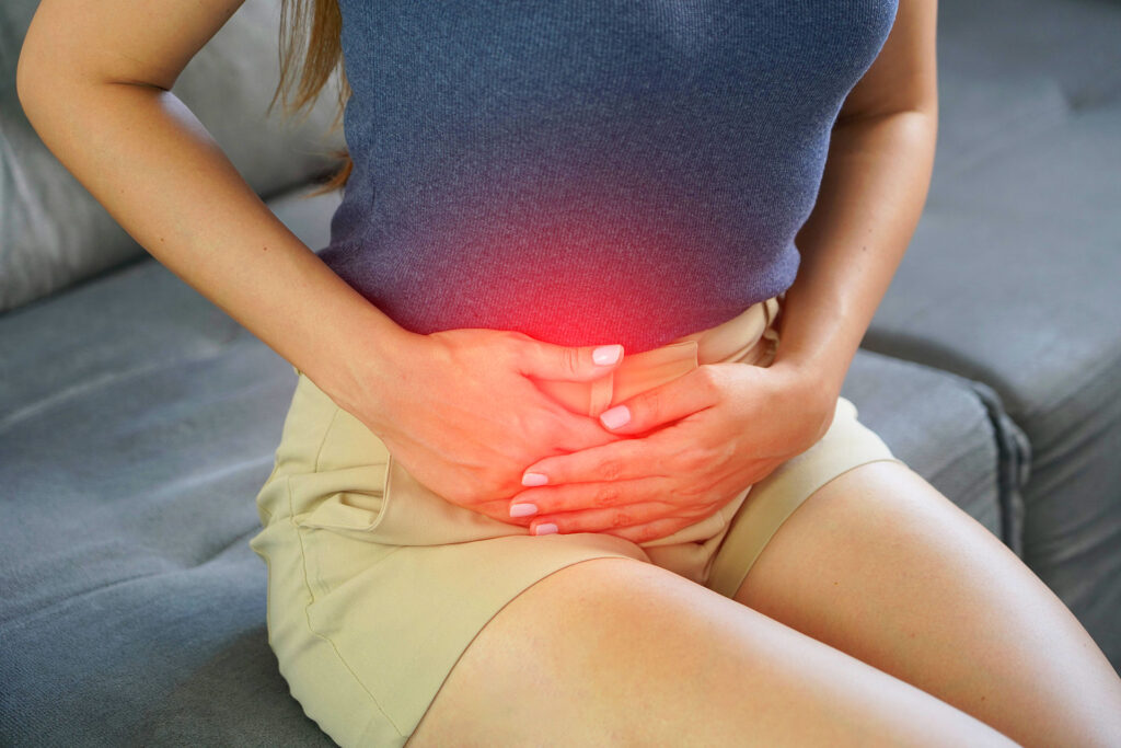 Close-up of a woman pressing her hands against a highlighted red area on her lower stomach, representing localized discomfort from pelvic congestion syndrome.