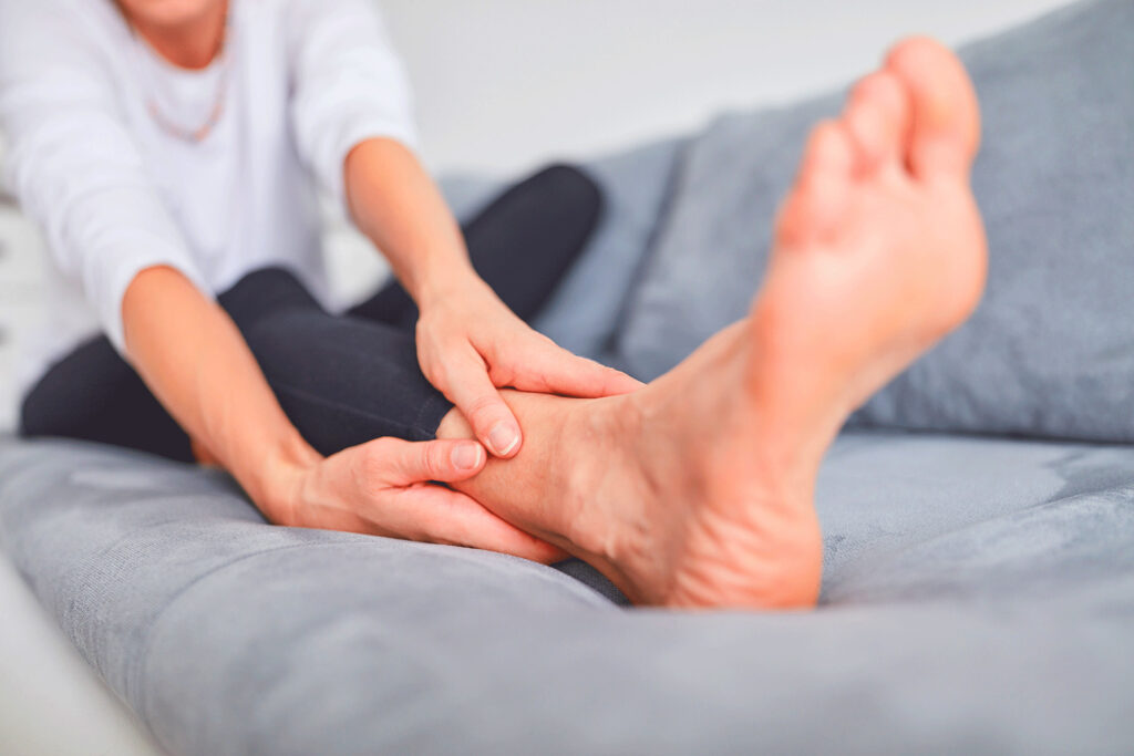 Woman sitting on a sofa and holding her ankle to relieve discomfort caused by pain in leg when lying down