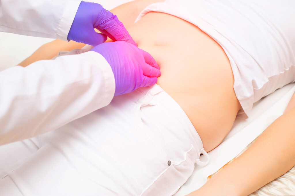 Doctor in medical gloves examining a patient's lower abdomen during a clinical checkup for pelvic congestion syndrome.