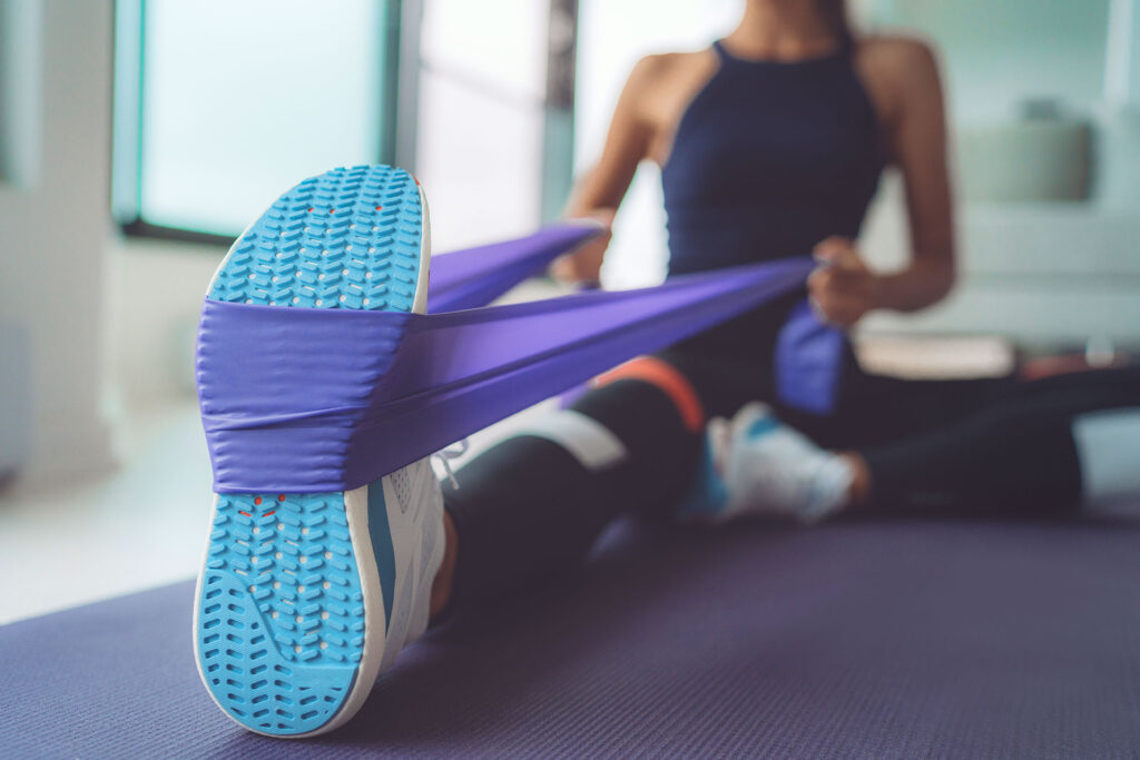 Athlete stretching her leg with a purple resistance band to improve circulation and reduce varicose veins from working out.