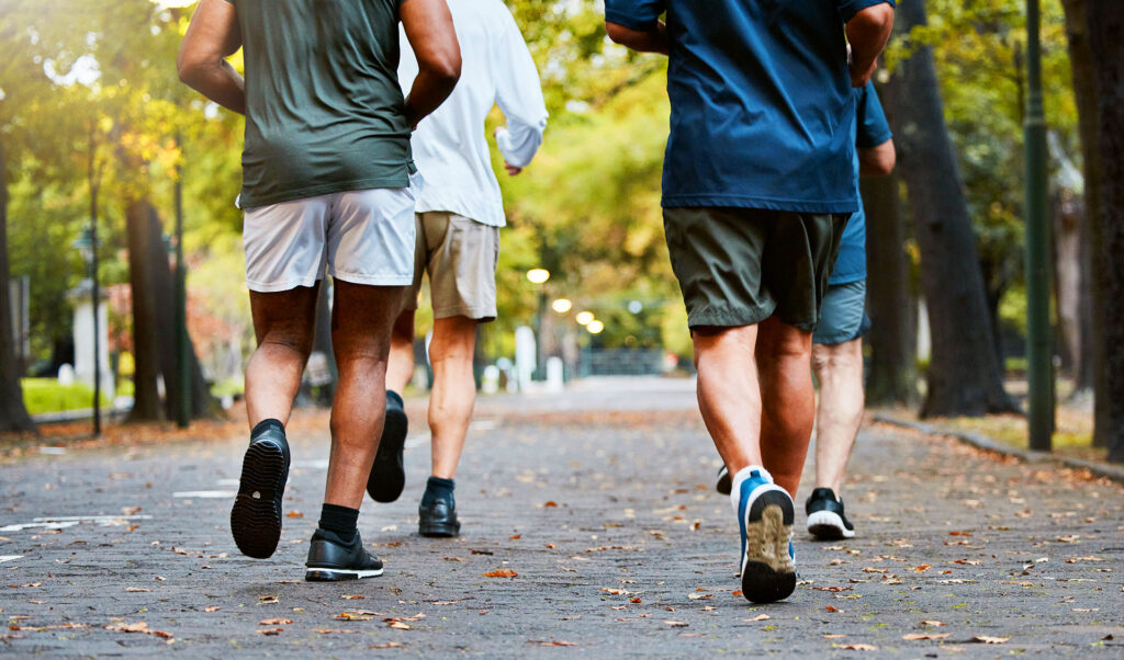Group of men running together in a park, illustrating cardiovascular exercise and preventing varicose veins from working out.
